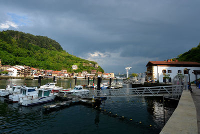 Boats moored at harbor by buildings against sky