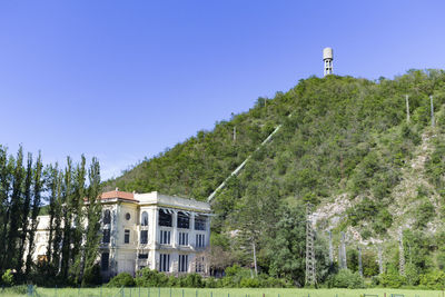 Building by mountain with water tower on top against clear blue sky