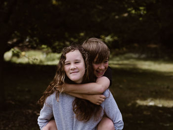 Portrait of smiling sister piggybacking brother in forest