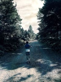 Rear view of man standing on road against trees