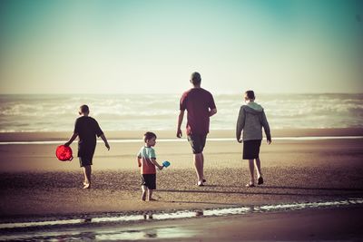 Rear view of people on beach against sky