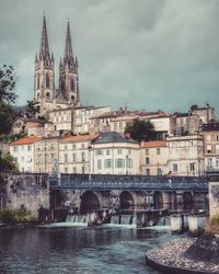 Arch bridge over river by buildings against sky