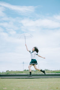 Full length of woman with arms raised on field against sky