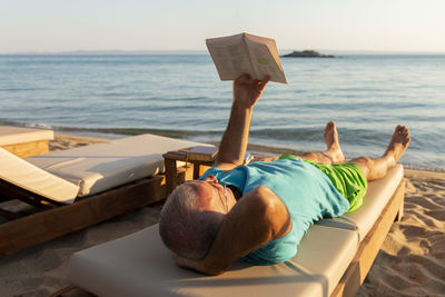 Mature man lying on a sunbed and reading a book at sunset. summer vacation concept.