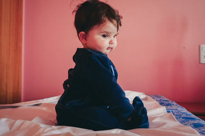 Cute boy looking away while sitting on bed at home