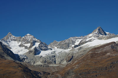 Low angle view of snowcapped mountains against clear blue sky