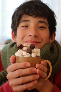 Close-up portrait of smiling boy holding mug of hot chocolate with marshmallows