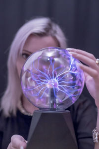 Close-up portrait of young woman holding plasma ball over black background