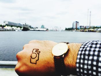 Close-up of hand against river in city against sky