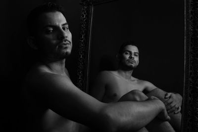 Shirtless young man standing from a mirror against black background