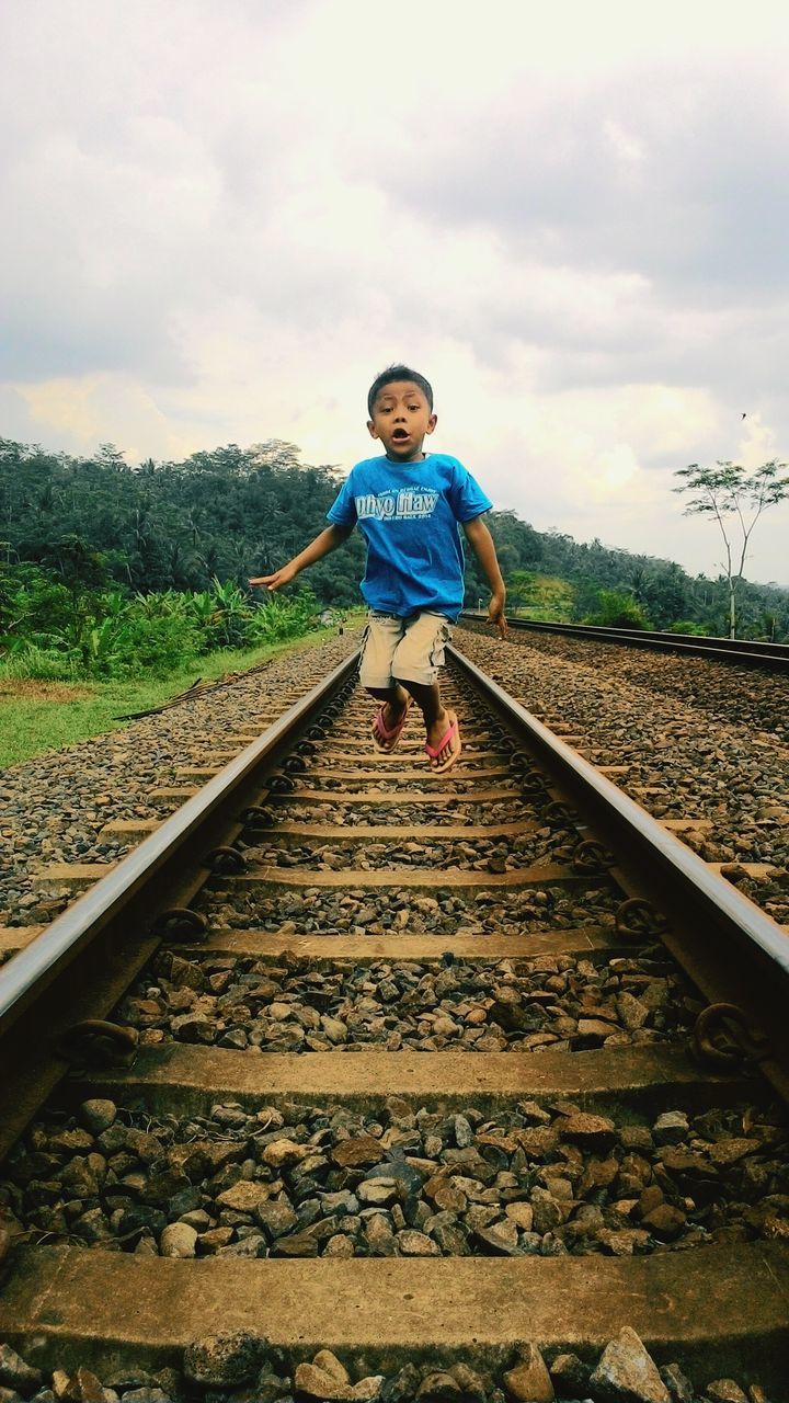 person, casual clothing, full length, sky, lifestyles, portrait, looking at camera, leisure activity, standing, front view, railroad track, cloud - sky, smiling, young adult, happiness, day, elementary age, childhood