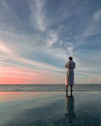 Rear view of man standing on beach against sky during sunset