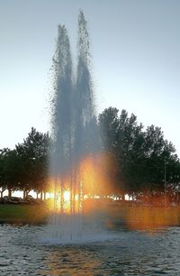 Fountain in lake against sky during sunset