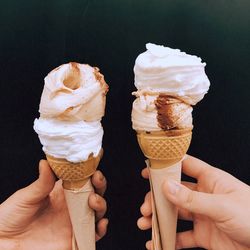 Cropped hands holding ice cream cones against black background