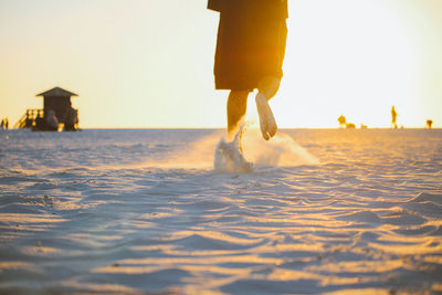 Low section of person on beach against sky during sunset