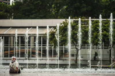 Rear view of woman sitting by fountain in city