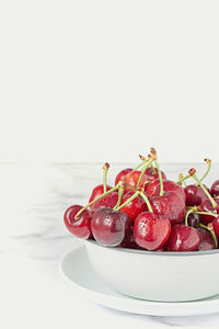 Fresh ripe red cherry with stalks in white ceramic pot placed on marble table against white wall