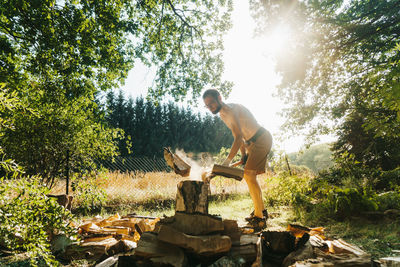 Full length of shirtless lumberjack cutting wood on field