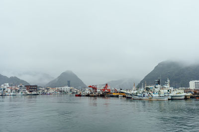 Sailboats in sea by harbor against sky