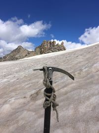 Ice axe and rope on snow against sky