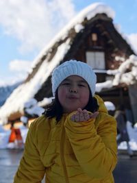 Portrait of cute girl blowing kiss while standing in snow