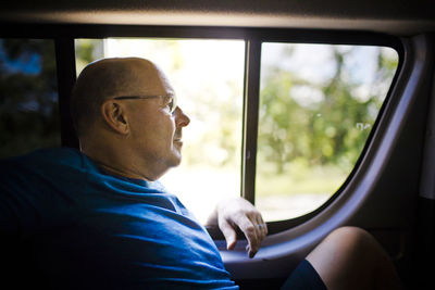 Relaxed retired man sits next to window in back of vehicle.