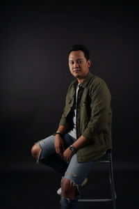 Portrait of young man sitting against black background