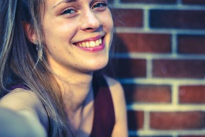 Close-up portrait of smiling woman against brick wall