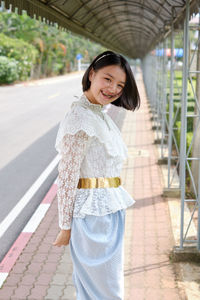 Portrait of young woman smiling while standing on sidewalk