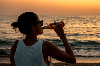 Man with arms raised on beach against sky during sunset