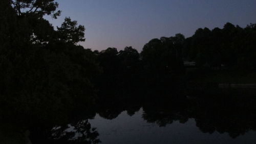 Reflection of silhouette trees in lake against sky