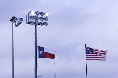 Low angle view of floodlights and flags against sky