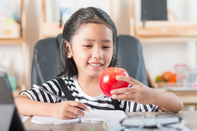 Girl holding toy while writing on book at table