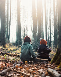 Rear view of kids sitting in forest during winter