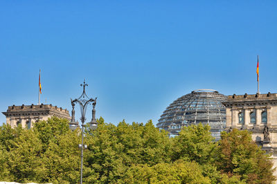 Low angle view of trees by the reichstag against clear blue sky