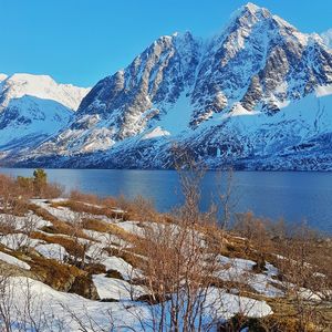 Frozen lake by snowcapped mountains against sky