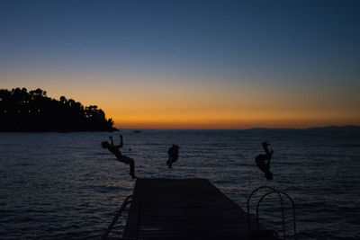Silhouette people on sea against sky during sunset