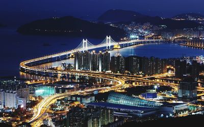 High angle view of illuminated city by sea against sky