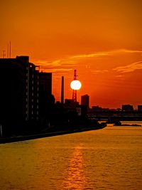 Silhouette buildings by sea against romantic sky at sunset