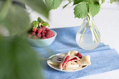 Slavic dish vareniki with fresh raspberries, still life on a blue background