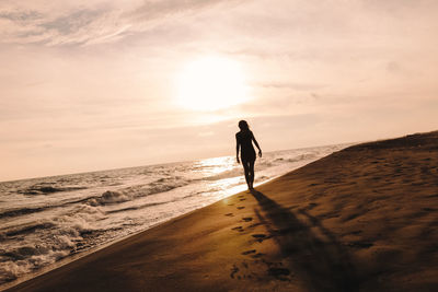 Silhouette man walking on beach against sky during sunset