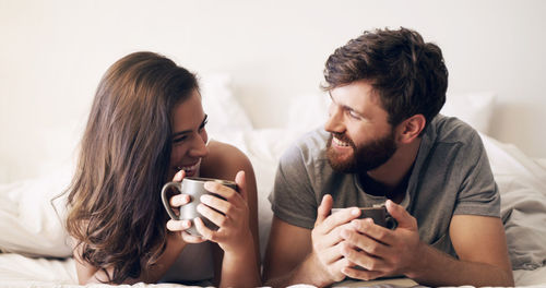 Happy couple with coffee cup lying on bed at home