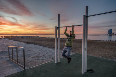 Rear view of man standing on beach against sky during sunset