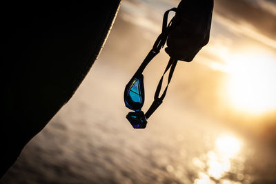 Midsection of woman holding goggles against sky during sunset