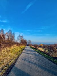 Empty road amidst field against sky
