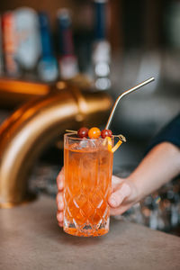 Crop anonymous person demonstrating transparent glass with cold cocktail with ice cubes served with berries on stick and zero waste straw person