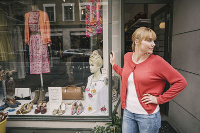 Confident owner standing against store looking away with hand on hip