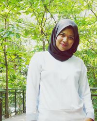 Portrait of young woman standing against trees