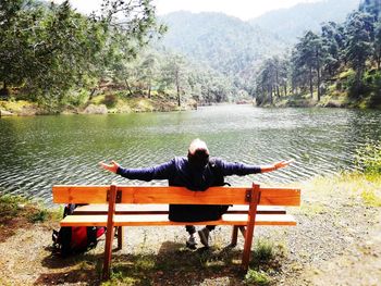 Man sitting on bench by lake against trees