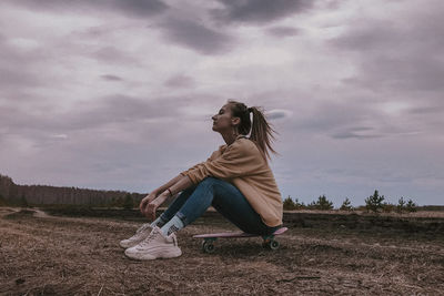 Side view of woman sitting on field against sky